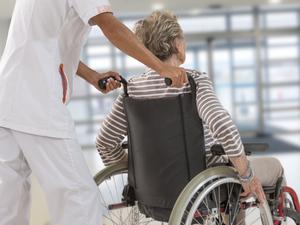 Eine alte Frau wird von Klinikpersonal in einem Rollstuhl geschoben.