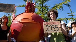 20.09.2025, Berlin: Eine Demonstrantin hält ein Plakat mit der Aufschrift „Gasausstieg 2035” während der Fridays for Future-Kundgebung am Invalidenpark in Berlin. Neben der Demonstrantin steht eine Person, verkleidet als eine brennende Erdkugel. 