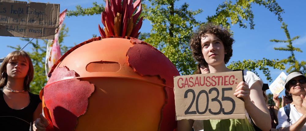 20.09.2025, Berlin: Eine Demonstrantin hält ein Plakat mit der Aufschrift „Gasausstieg 2035” während der Fridays for Future-Kundgebung am Invalidenpark in Berlin. Neben der Demonstrantin steht eine Person, verkleidet als eine brennende Erdkugel. 
