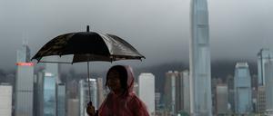 Ein Mädchen hält auf diesem Archivfoto einen Regenschirm in Tsim Sha Tusi vor dem Victoria Harbor und der Skyline von Hongkong.  