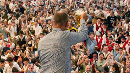 21.09.2025, Bayern, München: Bundeskanzler Friedrich Merz (CDU) prostet bei seinem Besuch des 190. Oktoberfest, auf Einladung von Bayerns Ministerpräsident Söder (CSU), mit einem Bierkrug den hunderten Bierzeltbesuchern von der Empore in der Festhalle Schottenhamel zu.