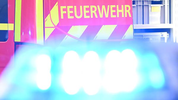 Ein Fahrzeug der Feuerwehr steht bei einem Einsatz auf einer Straße, während im Vordergrund das Blaulicht eines Polizeifahrzeugs zu sehen ist. (Symbolbild)