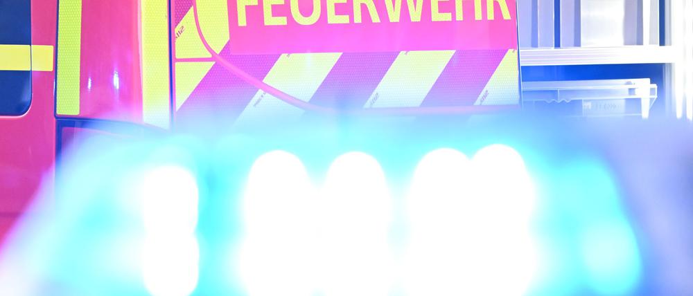 Ein Fahrzeug der Feuerwehr steht bei einem Einsatz auf einer Straße, während im Vordergrund das Blaulicht eines Polizeifahrzeugs zu sehen ist. (Symbolbild)