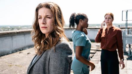 Dina Schwarz (Lou Strenger, links) blickt zu dem am Dach-Rand stehenden Nathan Freye. Im Hintergrund rufen Veronika Jelinek (Ulrike Tscharre, rechts) und Jenny de Luca (Melodie Simina, Mitte) Hilfe.