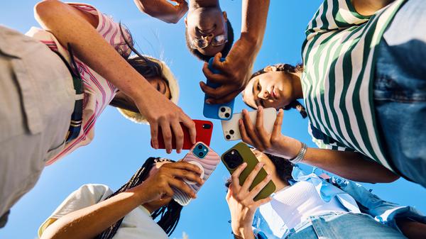 Five high school students are looking down at their smartphones together outdoors
