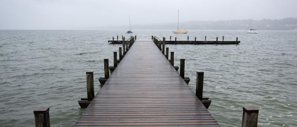Dunkle Wolken ziehen über einen Steg am Starnberger See. 
