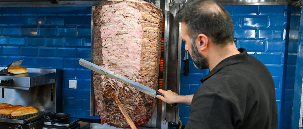 Ein Mann schneidet Fleisch von einem Döner-Spieß.