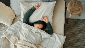 Eine junge Frau liegt rücklings mit ausgestreckten Armen auf dem Bett und schläft.