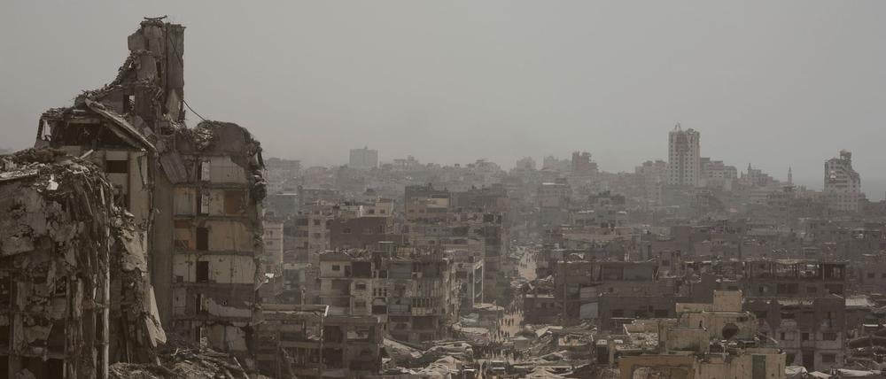 Menschen gehen im Gazastreifen eine Straße entlang, die von Gebäuden umgeben ist, die durch israelische Bombardierungen im Gazastreifen zerstört wurden.