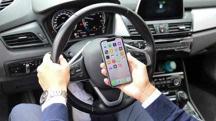 Ein Autofahrer schaut am Steuer auf ein Smartphone.