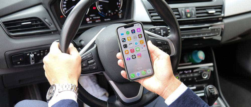Ein Autofahrer schaut am Steuer auf ein Smartphone.