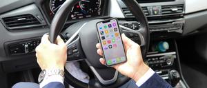 Ein Autofahrer schaut am Steuer auf ein Smartphone.
