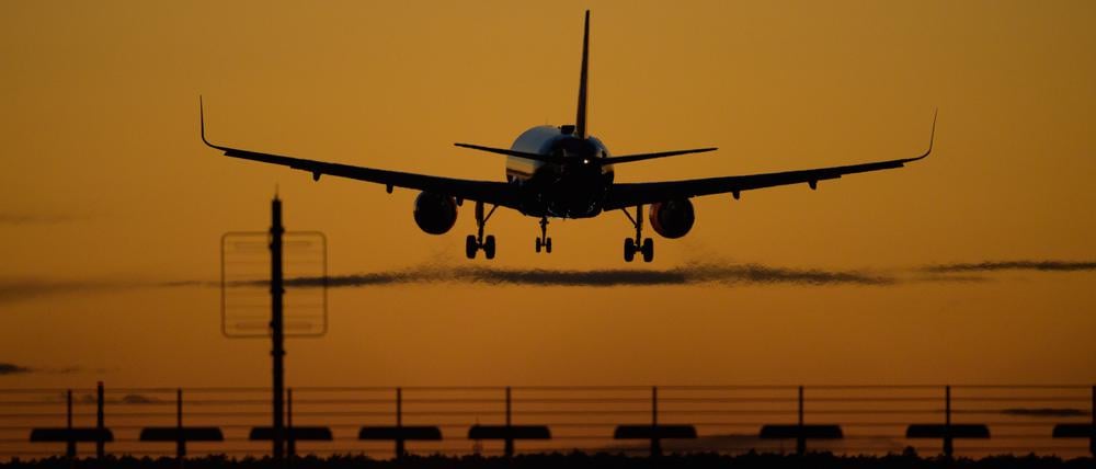 Ein Flugzeug landet auf dem Flughafen Berlin-Brandenburg (BER) vor rotem Abendhimmel.
