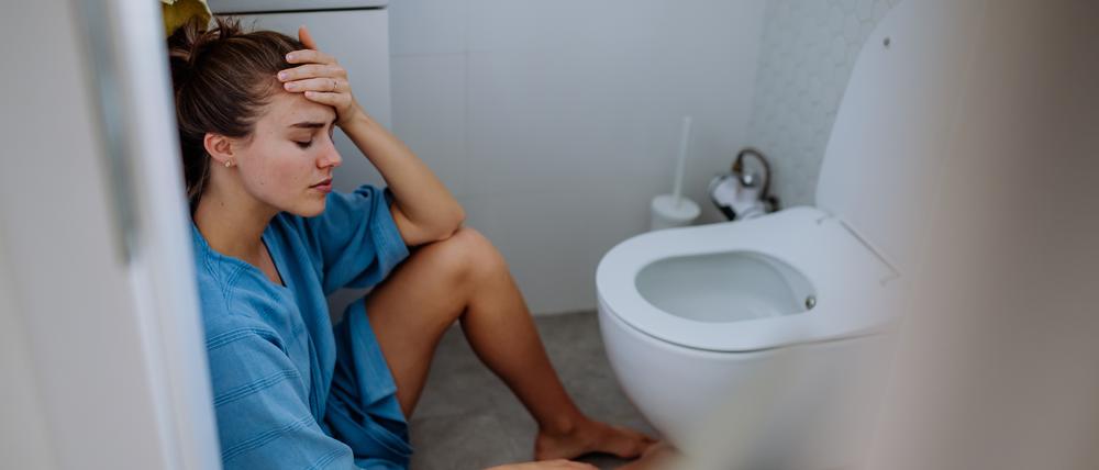 Eine junge Schwangere sitzt vor einer Toilette..