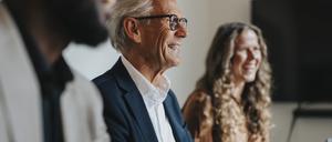 Ein älterer, fröhlicher Mann neben Kollegen im Büro