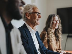 Ein älterer, fröhlicher Mann neben Kollegen im Büro