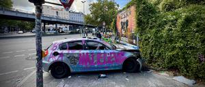 Ein schwer beschädigter, silberner, mit Graffiti und Aufkleber versehener BMW 1 steht quer auf einem Gehweg neben einer Ampel in der Audre-Lorde-Straße Ecke Oranienstraße.