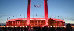 Das Olympiastadion in Berlin in roter Beleuchtung und vor blauem Himmel (Symbolbild)