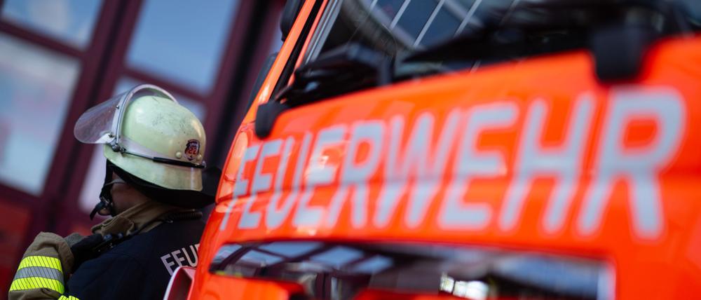 Eine Einsatzkraft der Feuerwehr steht neben einem Einsatzfahrzeug der Feuerwehr. 
