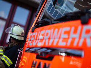 Eine Einsatzkraft der Feuerwehr steht neben einem Einsatzfahrzeug der Feuerwehr. 