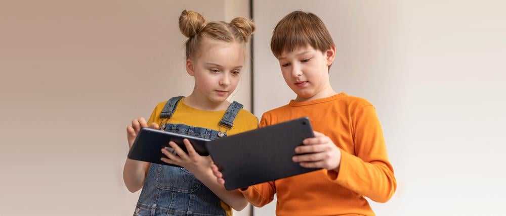 Ein Junge und ein Mädchen blicken auf ihre Tablets und lösen Aufgaben.
