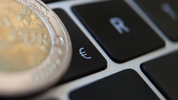 Eine Zwei-Euro-Münze liegt auf der Tastatur eines Laptops neben einem Eurozeichen.