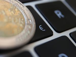 Eine Zwei-Euro-Münze liegt auf der Tastatur eines Laptops neben einem Eurozeichen.