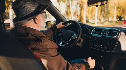 An elderly man wearing a hat enjoys a scenic urban drive during a sunny autumn day with vibrant foliage.