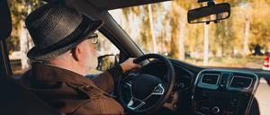 An elderly man wearing a hat enjoys a scenic urban drive during a sunny autumn day with vibrant foliage.