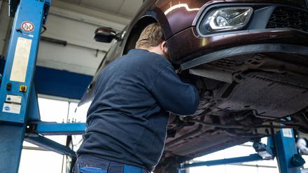 Ein Mechaniker schaut in den Radkasten eines Autos einer Kfz-Werkstatt in Berlin. 