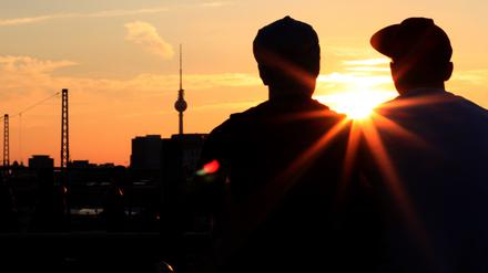 Zwei Männer sitzen beim Sonnenuntergang auf der Modersohnbrücke in Berlin.