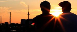 Zwei Männer sitzen beim Sonnenuntergang auf der Modersohnbrücke in Berlin.