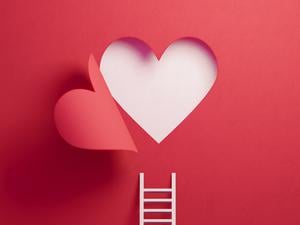White ladder leaning on red wall with cut out heart shape. Horizontal composition with copy space.