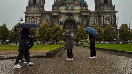 Menschen stehen in Regenkleidung und mit Schirmen vor dem Dom. 