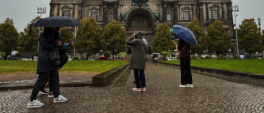 Menschen stehen in Regenkleidung und mit Schirmen vor dem Dom. 