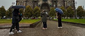 Menschen stehen in Regenkleidung und mit Schirmen vor dem Dom. 