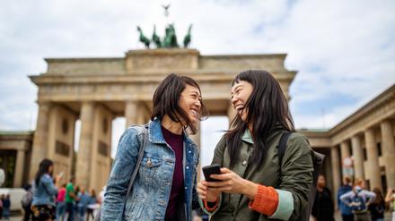 Zwei Touristinnen stehen lachend vor dem Brandenburger Tor.