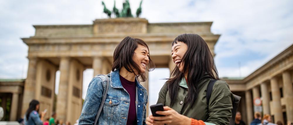 Zwei Touristinnen stehen lachend vor dem Brandenburger Tor.