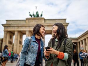 Zwei Touristinnen stehen lachend vor dem Brandenburger Tor.