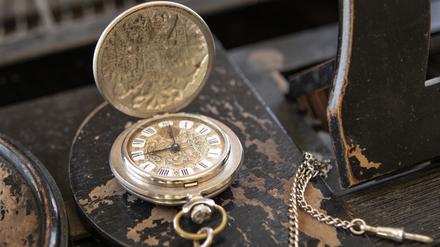 Eine Vintage-Uhr liegt aufgeklappt auf einem alten Holztisch.