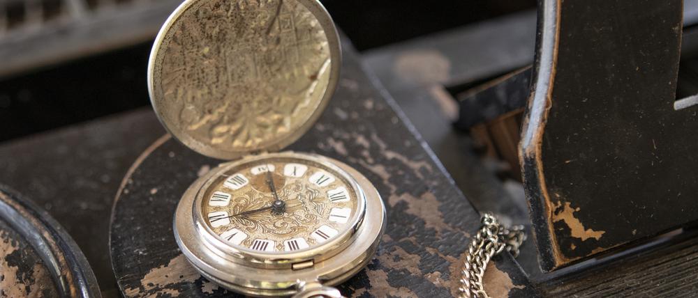 Eine Vintage-Uhr liegt aufgeklappt auf einem alten Holztisch.