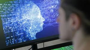 Ein Mann vor einem Bildschirm mit einem Kopf aus Daten (Symbolbild).