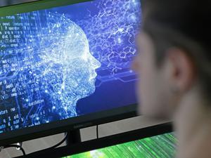 Ein Mann vor einem Bildschirm mit einem Kopf aus Daten (Symbolbild).