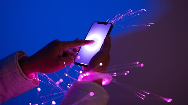 Hände streichen auf einem Handy-Display, Licht-Funken kommen heraus. Ein KI-generiertes Symbolbild für das Thema Digitalisierung. 