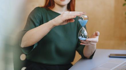 Woman in green shirt holding an hourglass at a table with a laptop model released, Symbolfoto property released, YTF03562