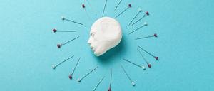 Illustration: Ein Kopf umgeben von Stecknadeln auf türkisfarbenem Hintergrund.