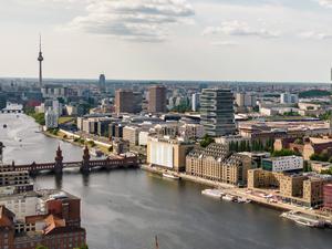 Drohenansicht auf die Berliner Spree mit dem Badeschiff unten, Amazon-Tower rechts und dem Fernsehturm oben.