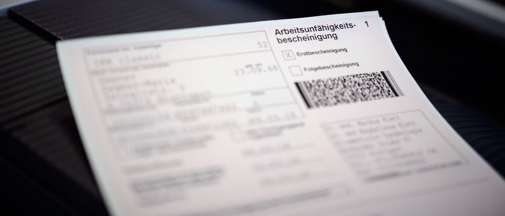 Eine Arbeitsunfähigkeitsbescheinigung liegt auf dem Drucker in einer Arztpraxis.