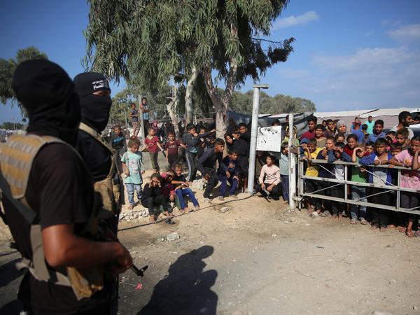 Palestinian Hamas militants stand guard as people gather to watch Red Cross vehicles transport hostages, held in Gaza since the deadly October 7, 2023 attack, following their handover as part of a ceasefire and hostages-prisoners swap deal between Hamas and Israel, in the central Gaza Strip, October 13, 2025. REUTERS/Stringer 