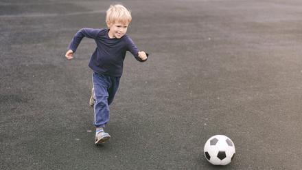 Ein Kind mit kurzen blonden Haaren läuft auf einen Fußball zu.